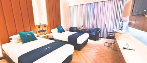 A hotel room with two beds, a desk, a chair, a TV, and a curtain.