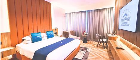 A hotel room with a large bed, a desk, a chair, a TV, and a view of the city center.