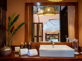 Un baño con un espejo grande, un lavamanos blanco y artículos de aseo en la encimera.