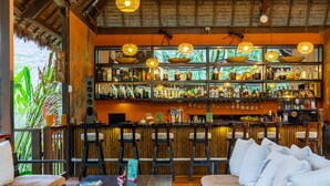 Zona de bar con muebles de madera, una variedad de botellas y luces colgantes.
