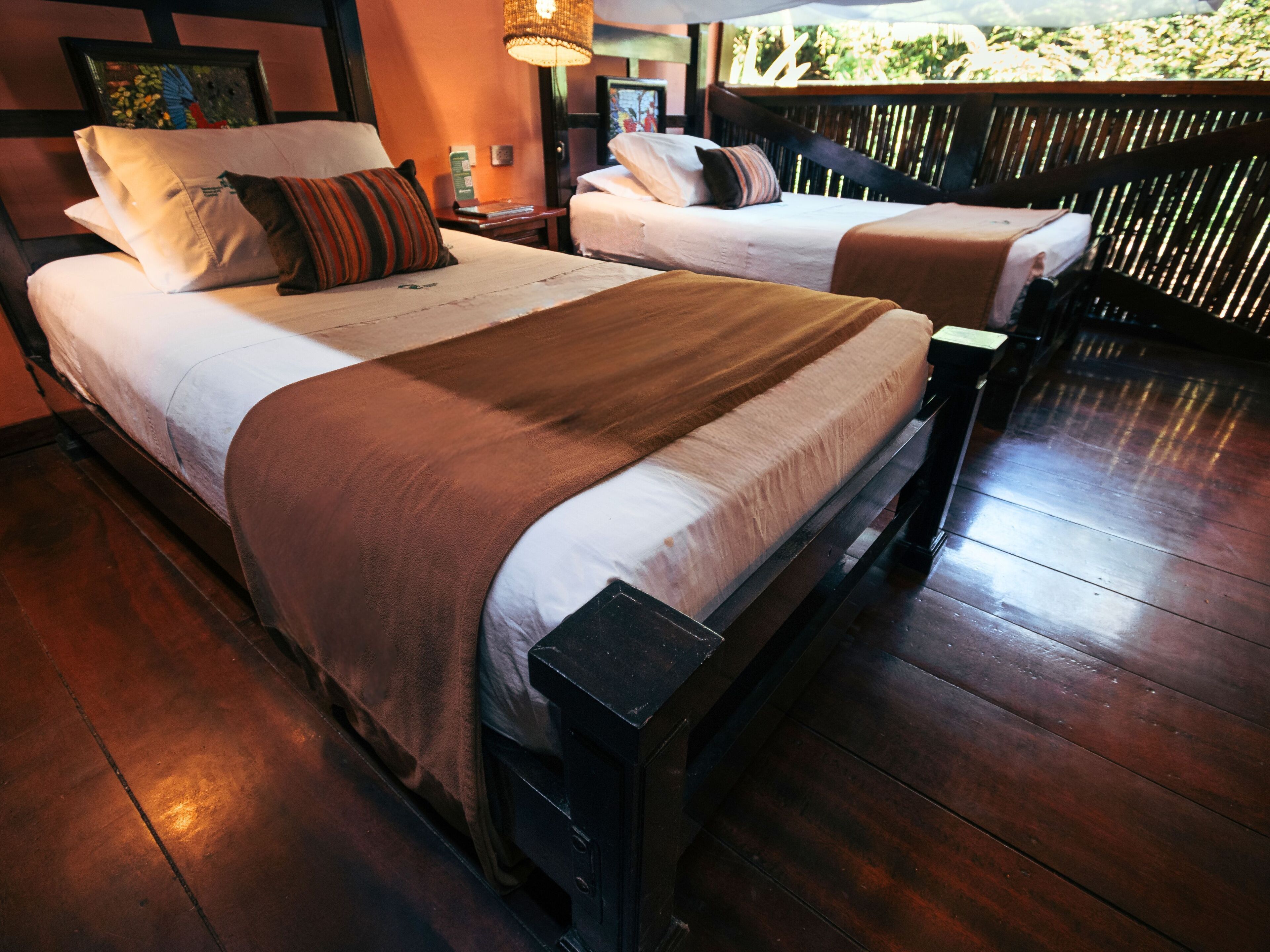 A double bed with a brown bedspread and a single bed with a white bedspread in a room with wooden flooring and a wooden headboard.