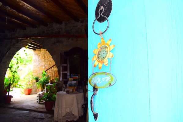 An arched stone doorway leading to a garden with potted plants and a table. - Vasilopoulos House (Tochni)
