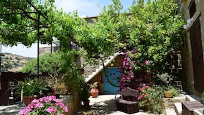Un cortile con pareti in pietra, piante in vaso, una panchina e una scala che porta a una porta.