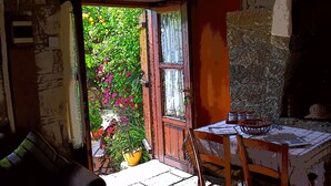 Una stanza rustica con una porta in legno che si apre su un giardino, un tavolo con un cesto e una finestra vista sul verde.