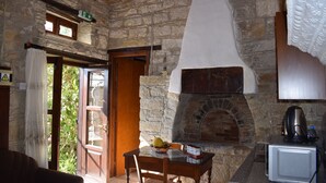 Una stanza con pareti in pietra, un camino, un tavolo con una ciotola di frutta e un piccolo elettrodomestico bianco.