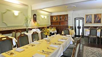 A formal dining room with long tables set for a meal, wooden paneling, and traditional decor.
