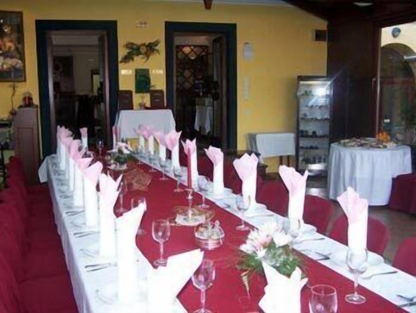 Une longue table à manger, recouverte de nappes blanches, agrémentée de serviettes roses et de verres à vin, dans une pièce aux murs jaunes et aux chaises rouges.