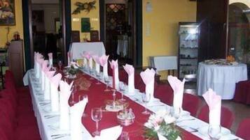 Une longue table à manger, recouverte de nappes blanches, agrémentée de serviettes roses et de verres à vin, dans une pièce aux murs jaunes et aux chaises rouges.