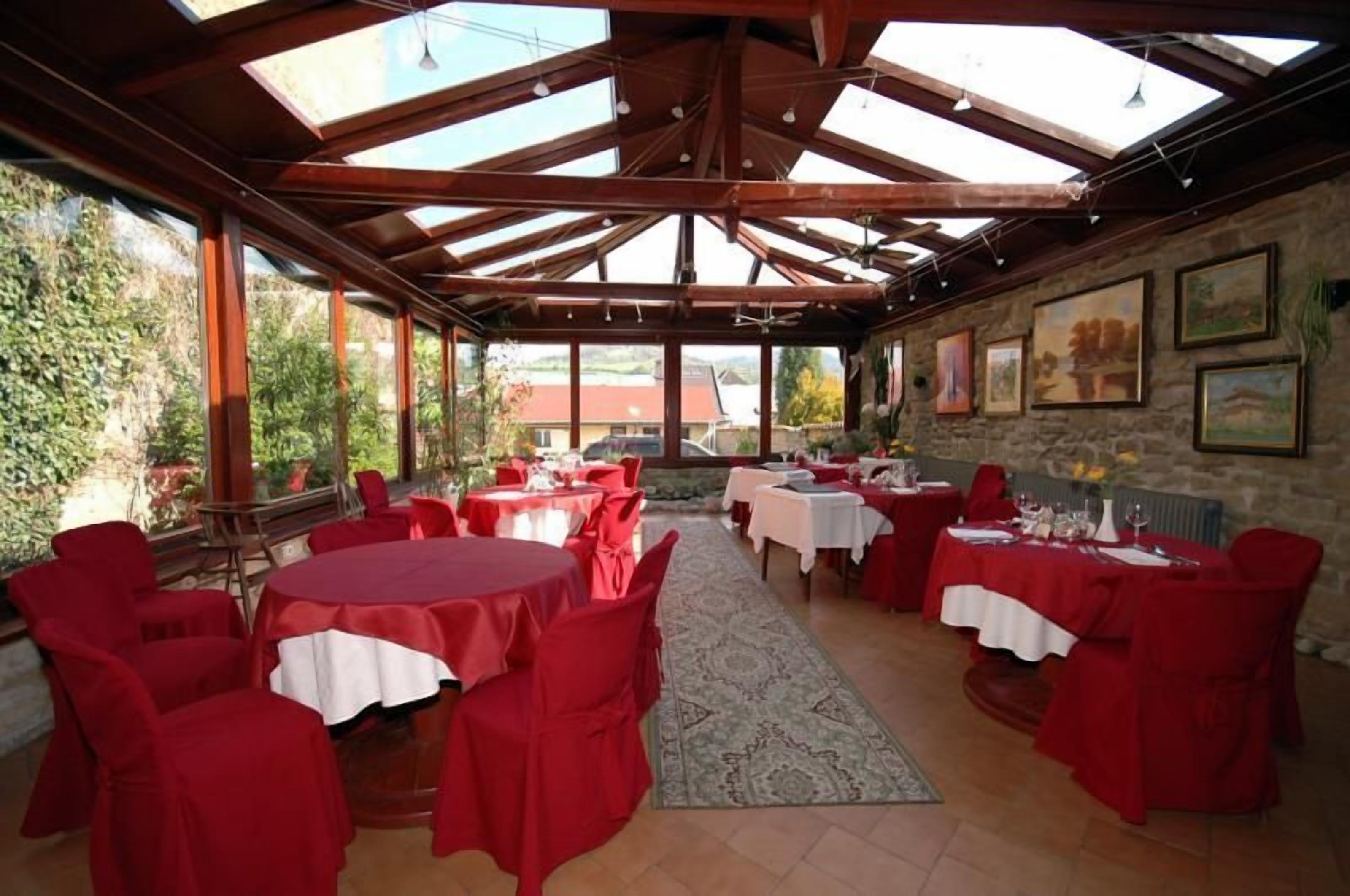 A covered dining area with tables and chairs, large windows, and artwork on the walls.