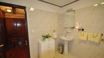 Un baño con puerta de madera, lavamanos, espejo y un cubo de basura.