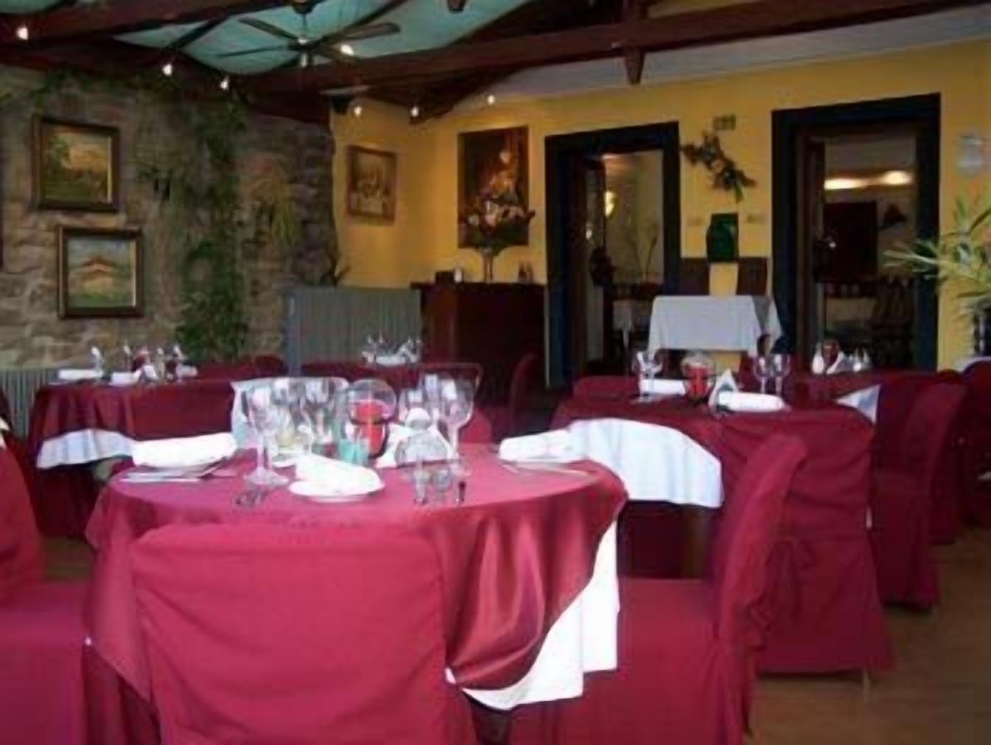 A restaurant with round tables covered in red tablecloths, each set with wine glasses and plates.