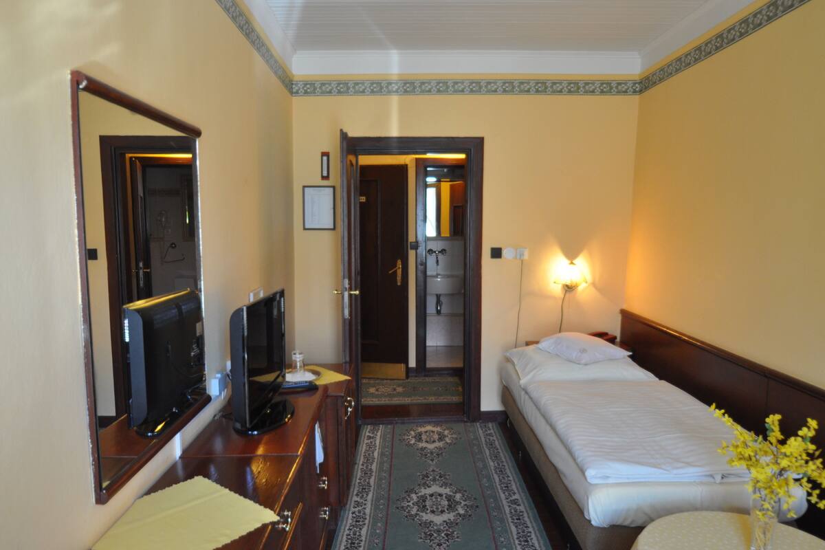 Een hotelkamer met een bed, een bureau met een computer, een spiegel, een deur en een wandlamp.