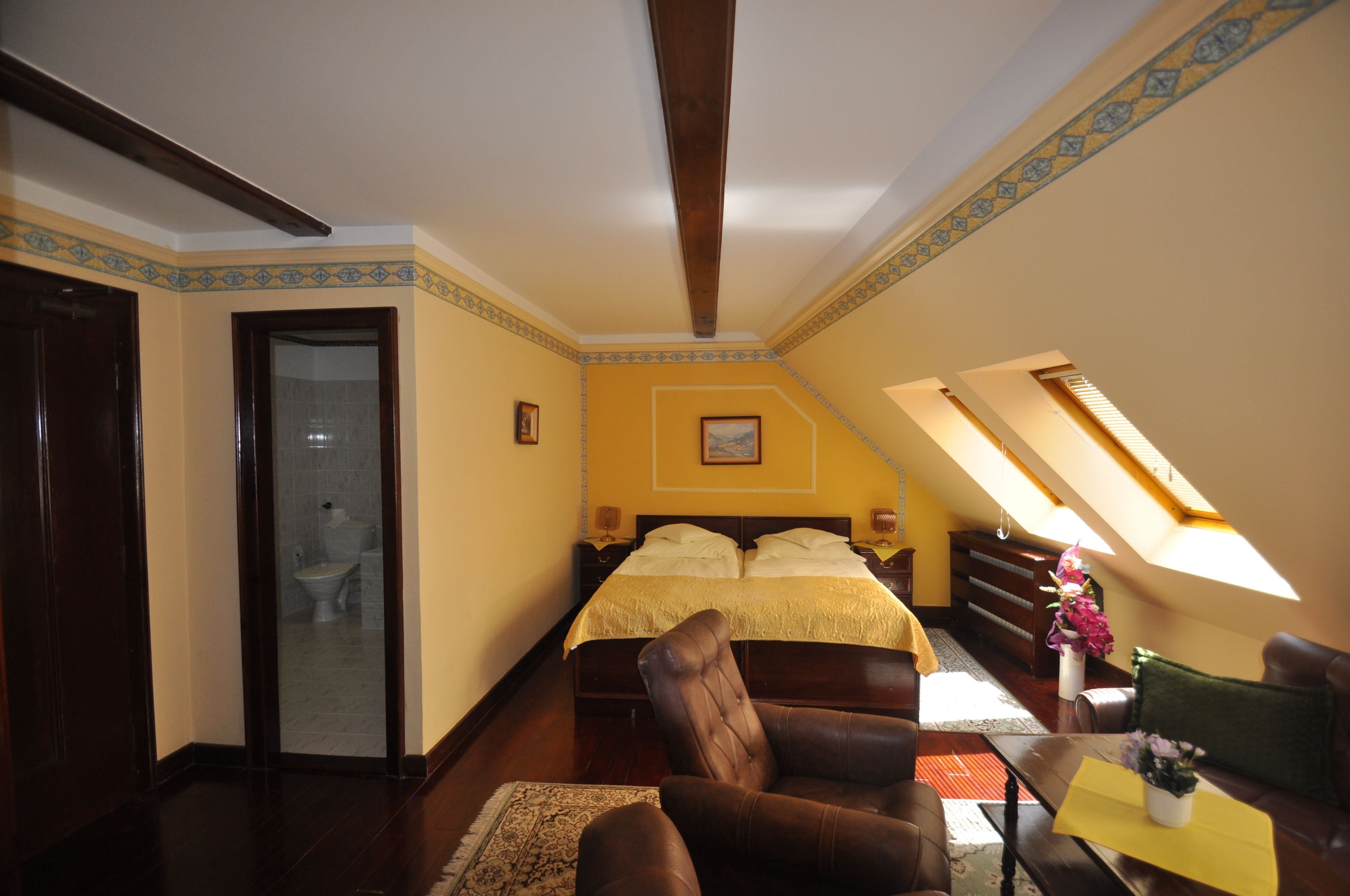 A bedroom with a large bed, a chair, a table with a vase, and a skylight.