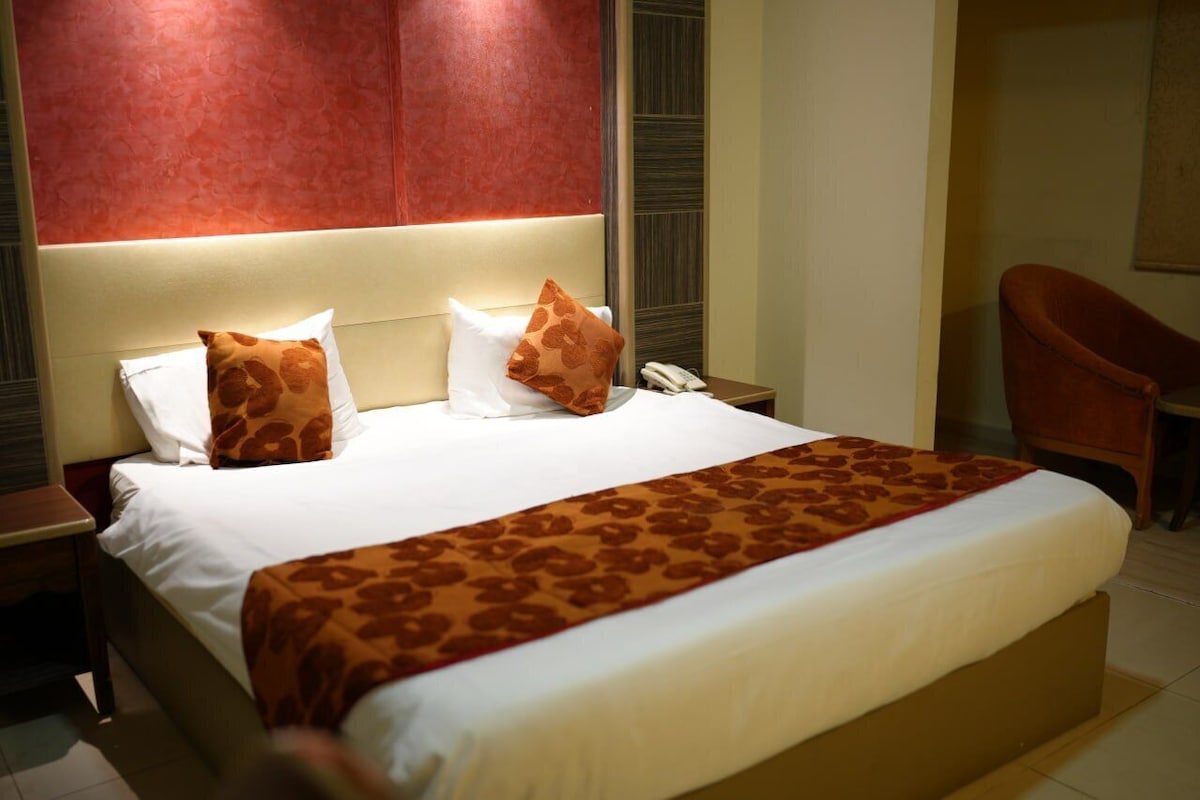 A hotel room with a large bed, a bedside telephone, and a chair.