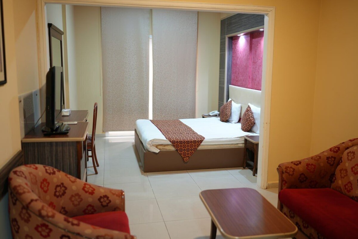 A hotel room with a bed, a desk with a computer, a chair, and a sofa.