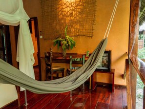 A hammock in a room with a wooden floor, a dining table, chairs, a plant, and a wall with a textured pattern.