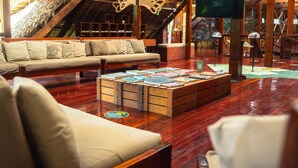 Un coin salon accueillant avec une table basse en bois sur laquelle sont posés des livres, un canapé avec des coussins et un téléviseur fixé au mur.