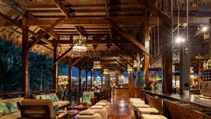 Un vaste espace intérieur doté de poutres en bois et d’un comptoir de bar, avec des coins salon aménagés et une vue sur l’extérieur.