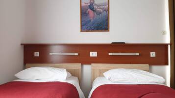 A hotel room with two beds, each with a red bedspread and white pillows, a wooden headboard with bedside tables, and a framed picture on the wall.