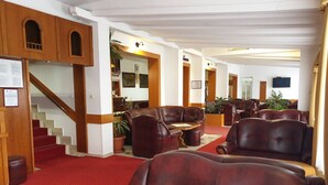 A hotel lobby with leather seating, a staircase, and a red carpet. - Hotel Mirni Kutak (Otocac)