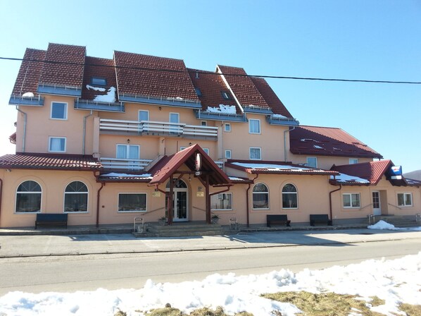 A multi-story building with a red-tiled roof, a central entrance with a small porch, and a staircase leading to the upper floors.