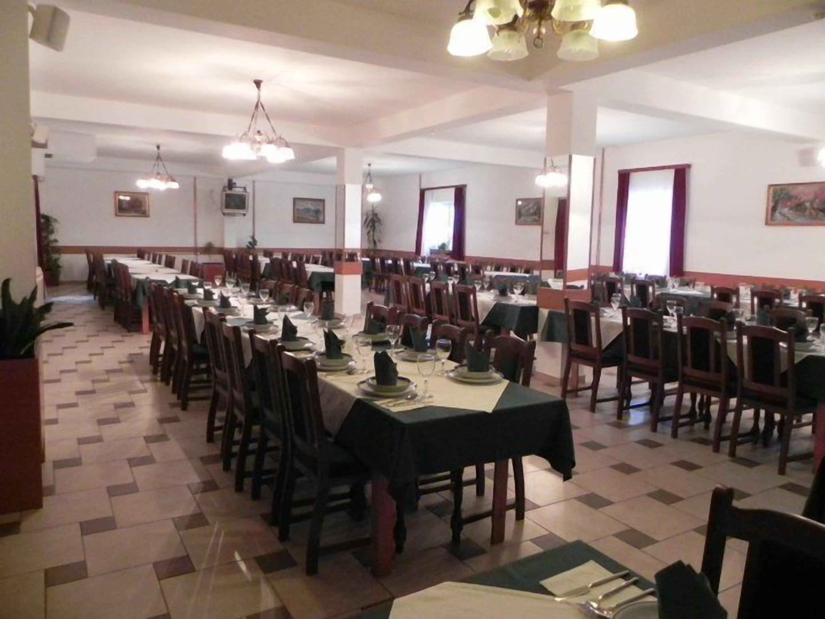 A large dining hall with multiple tables and chairs, high ceilings, and chandeliers.
