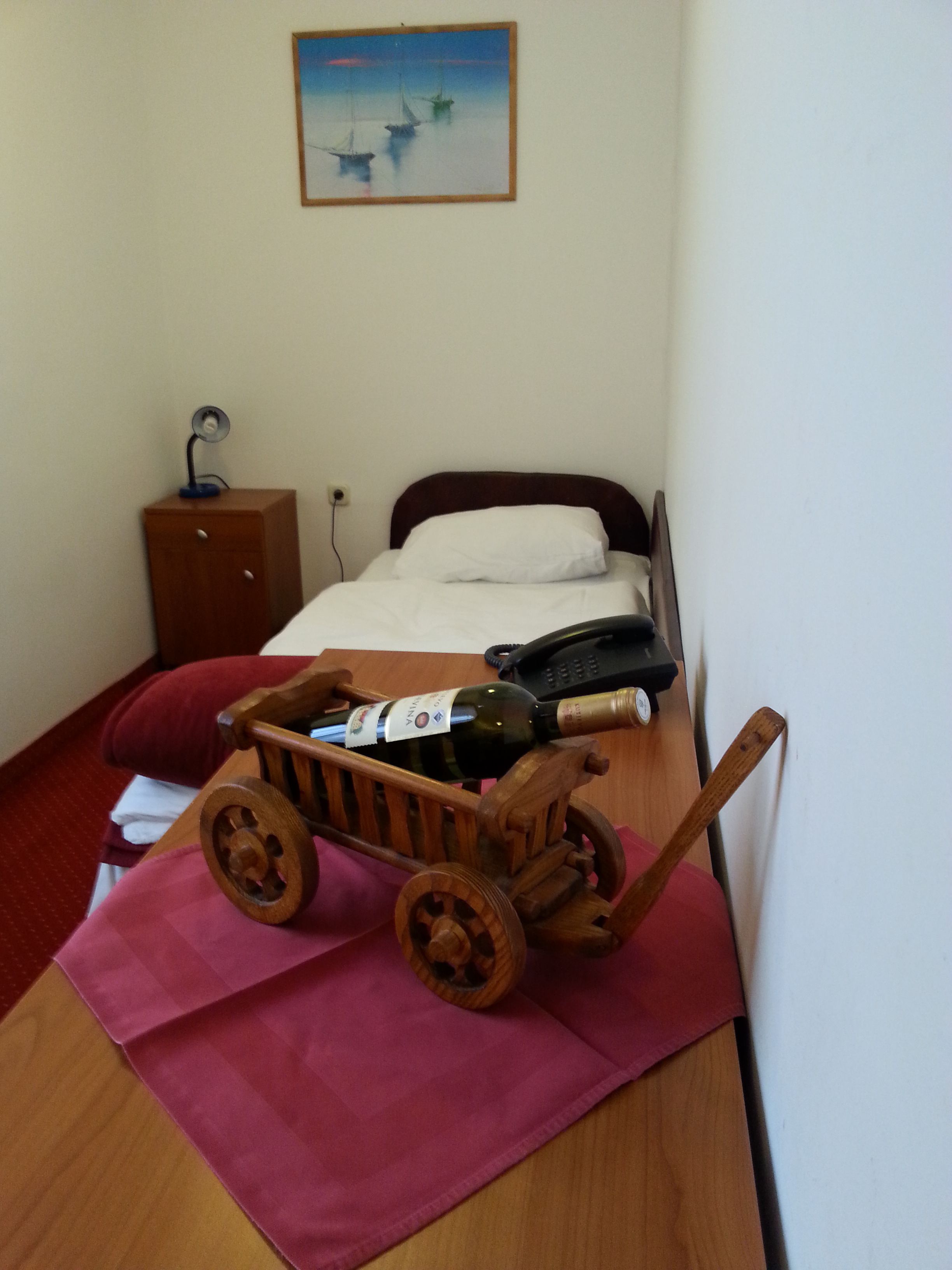 Un dormitorio con un carrito de madera, una cama, una mesita de noche, una lámpara y un cuadro en la pared.