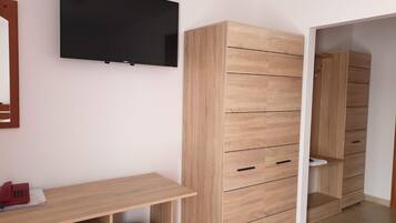 Una habitación con un escritorio de madera, un armario grande y un televisor montado en la pared.