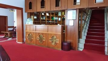 A reception area with a wooden counter, a staircase, and a red carpeted floor.