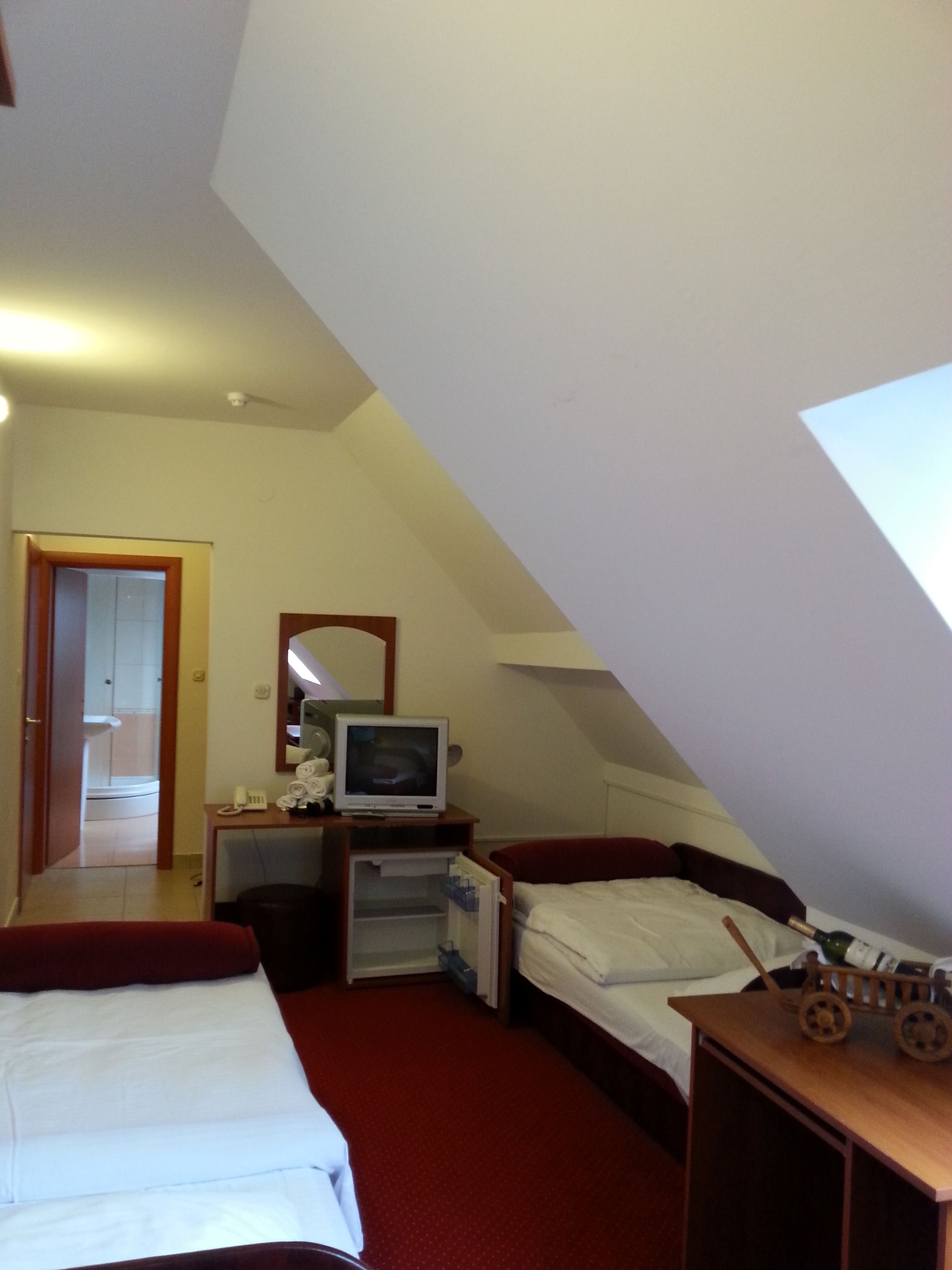 Een kleine, schuine kamer met een bed, een bureau met een computer, een spiegel en een houten speelgoedje op het bureau.