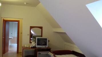 Een kleine, schuine kamer met een bed, een bureau met een computer, een spiegel en een houten speelgoedje op het bureau.
