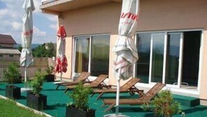 A poolside area with lounge chairs and umbrellas, a covered seating area, and a building with large windows. - Hotel Mirni Kutak (Otocac)