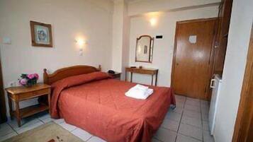 A bedroom with a bed, a wooden desk, a chair, a mirror, and a door.