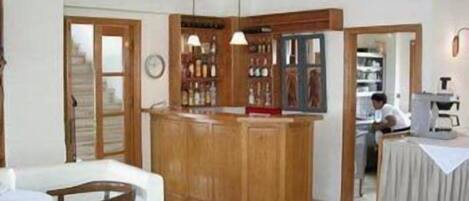 A room with a wooden bar area, a dining table with chairs, and a kitchen area with a person working.