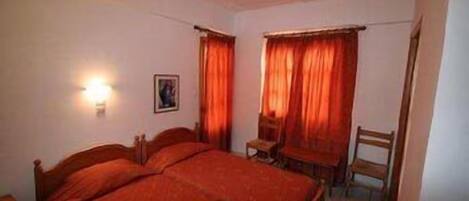 A bedroom with two single beds, a small table, a chair, and a wall-mounted light.