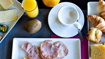 A breakfast setting with ham, eggs, orange juice, and croissants on a table.