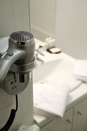 Un sèche-cheveux fixé au mur dans une salle de bain, avec un comptoir blanc et une serviette.