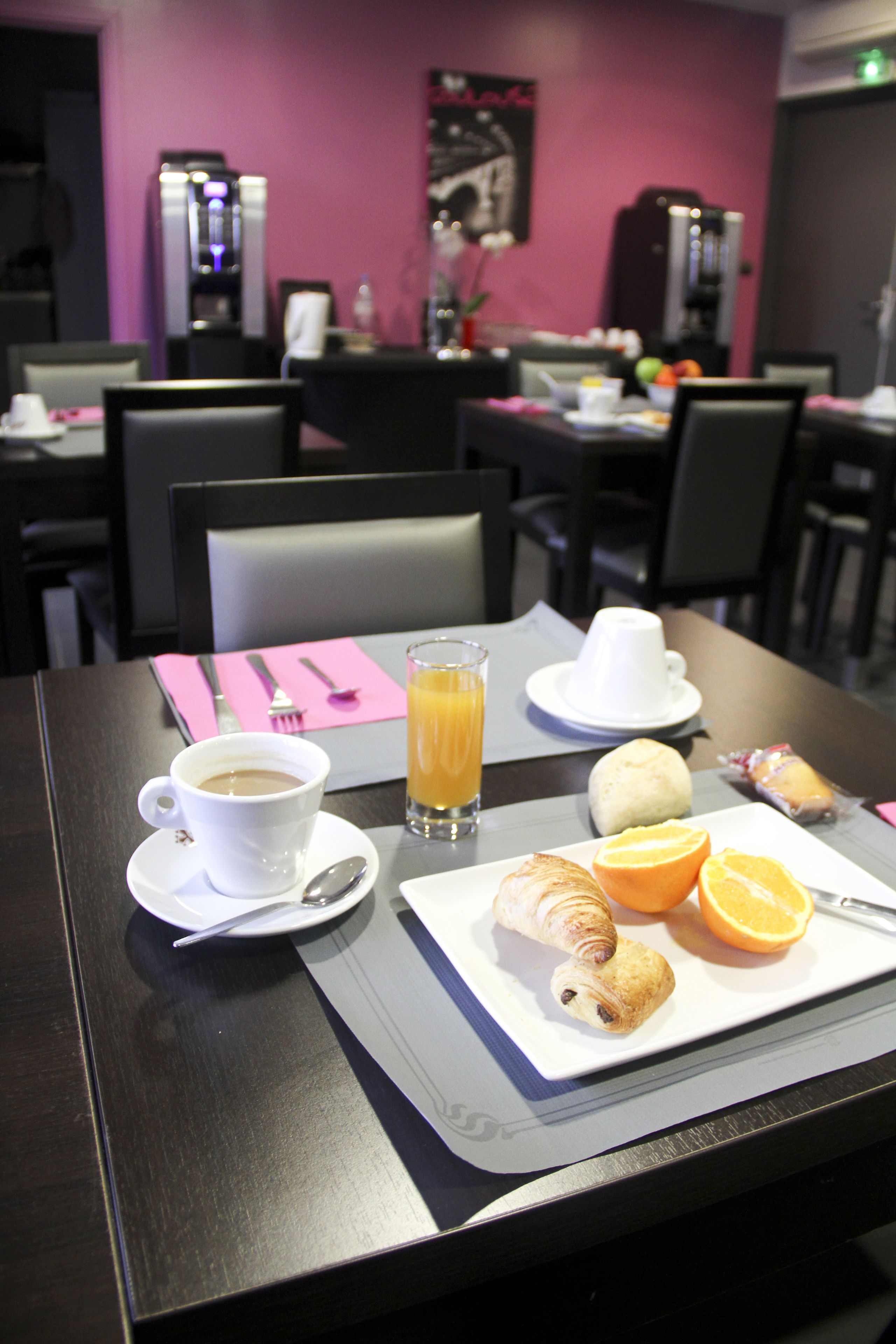 Une table de petit-déjeuner avec une tasse de café, du jus d’orange, des croissants et des tranches d’orange.