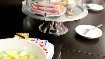 A buffet setup with a covered ham dish, a bowl of fruit salad, and a small plate with a fork.