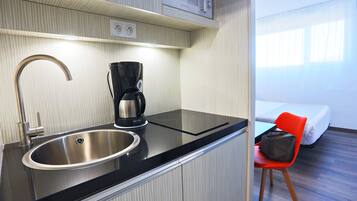 Een kleine keuken met een RVS spoelbak, een koffiezetapparaat en een magnetron erboven.