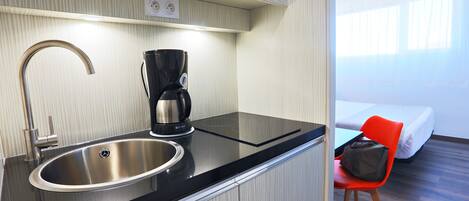 Une petite cuisine équipée d’un évier en acier inoxydable, d’une machine à café et d’un four à micro-ondes placé au-dessus.