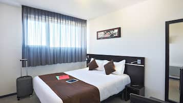 Une chambre d’hôtel avec un grand lit, une table de chevet, une valise, une fenêtre avec des rideaux et un tableau accroché au mur.