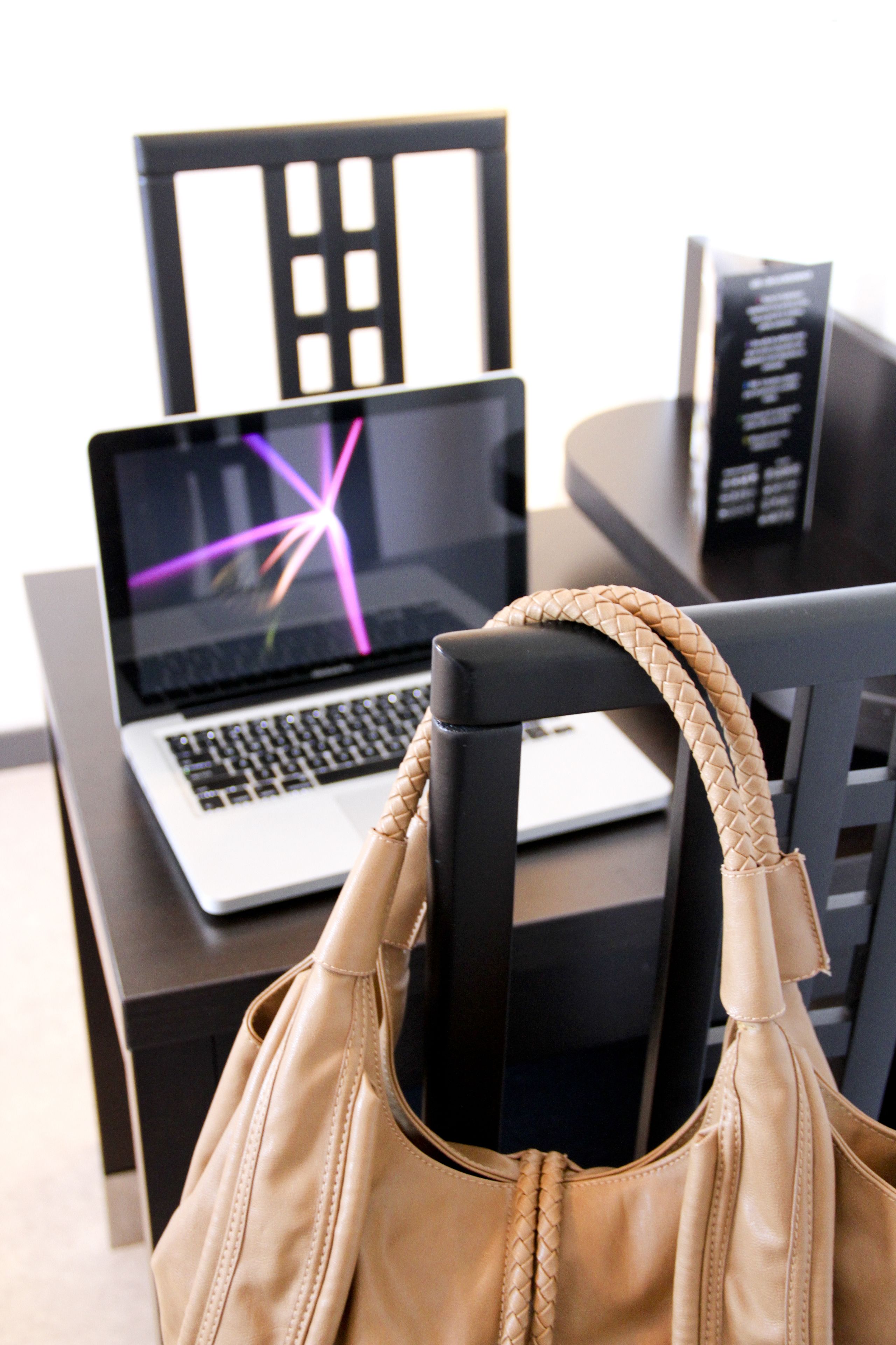 A laptop on a table with a beige handbag in front of it.