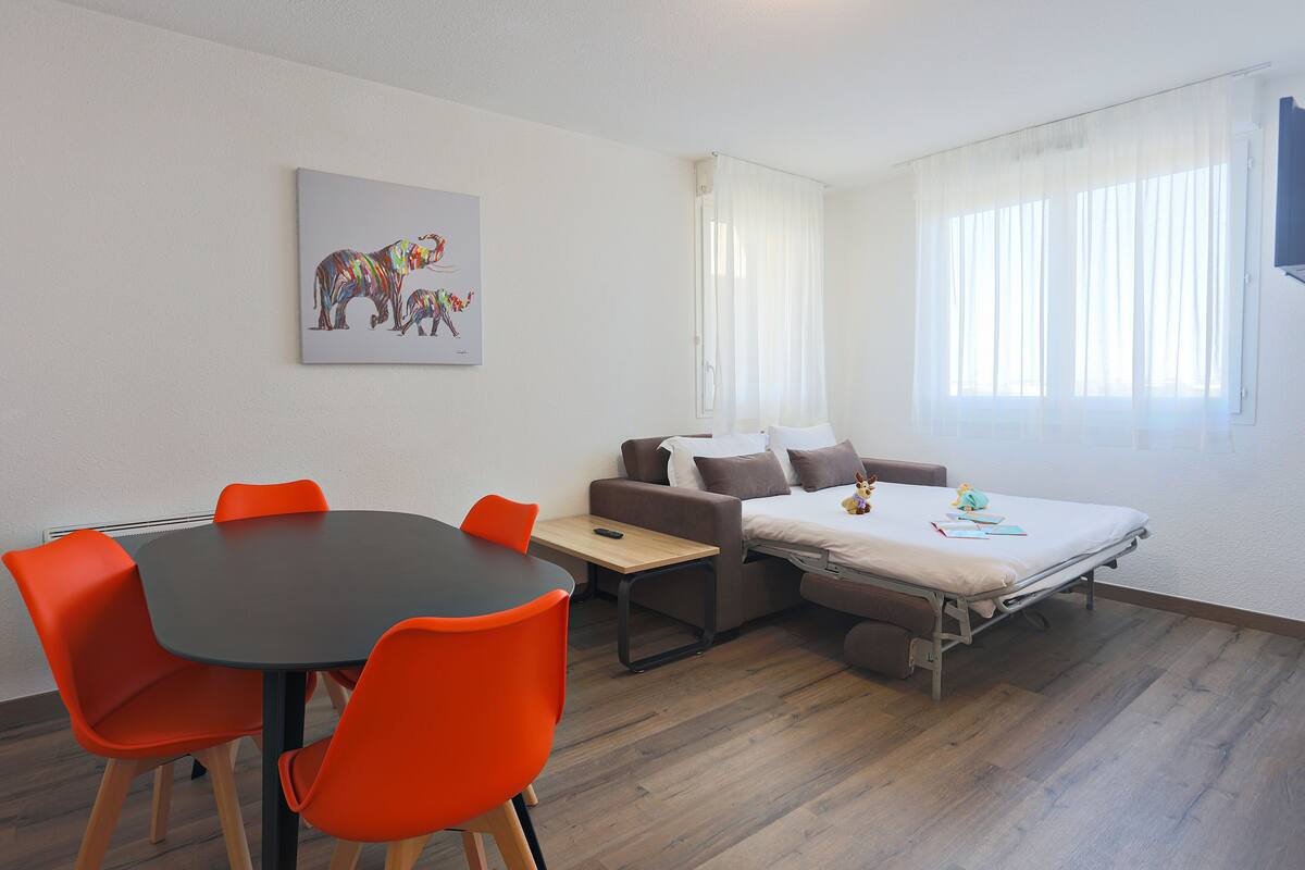 Un espace de vie compact comprenant un lit, un canapé, une table à manger avec des chaises et un tableau accroché au mur.