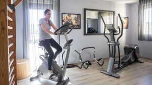 Ein Heimfitnessraum mit Trainingsgeräten, darunter ein Crosstrainer, ein Ergometer und ein Laufband.
