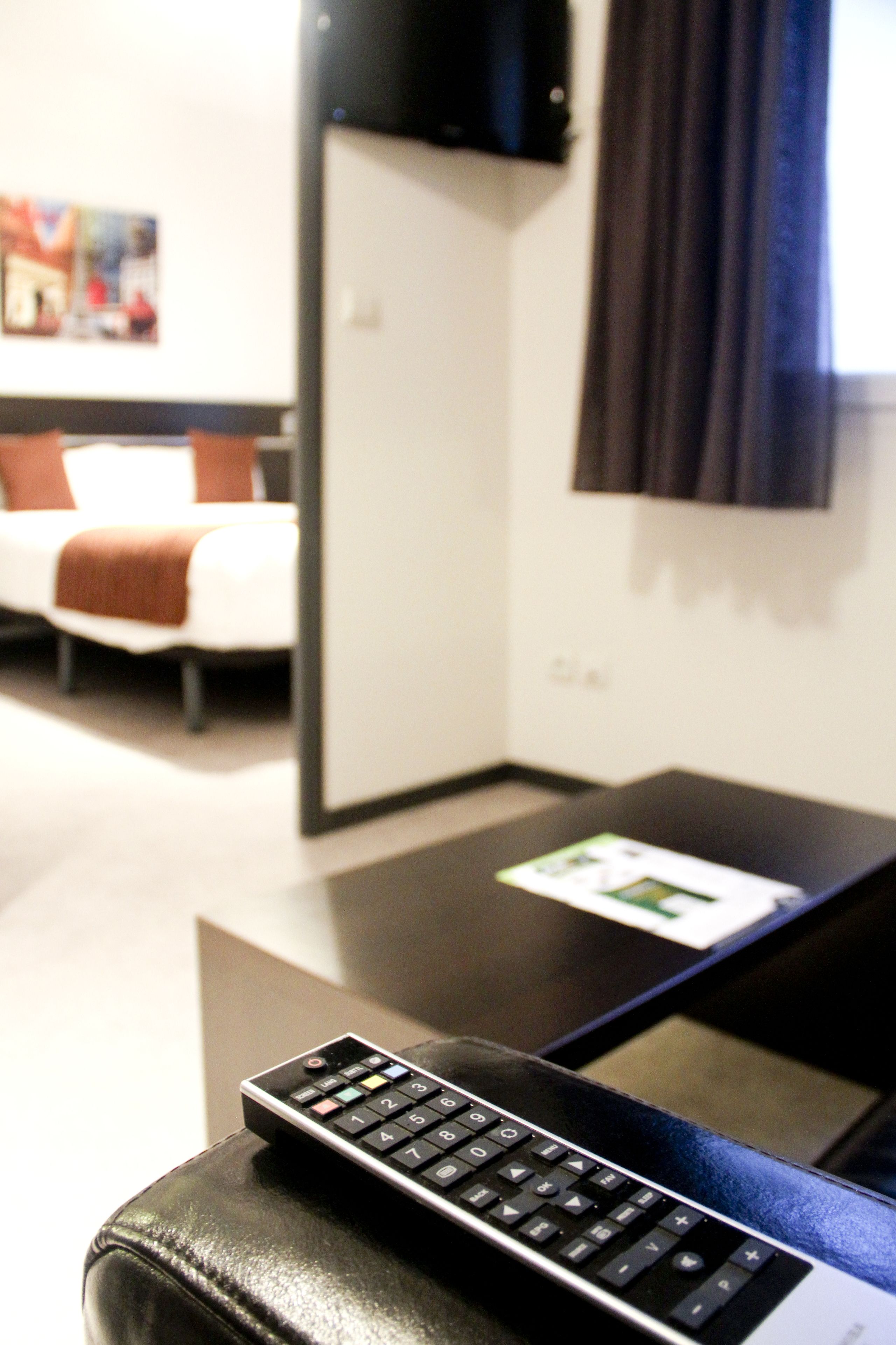 A remote control on a leather ottoman in a hotel room.