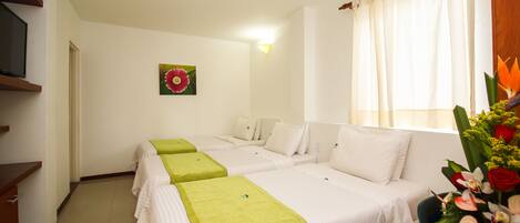Habitación de hotel con dos camas individuales, un escritorio, una silla, un televisor y una ventana con cortinas.