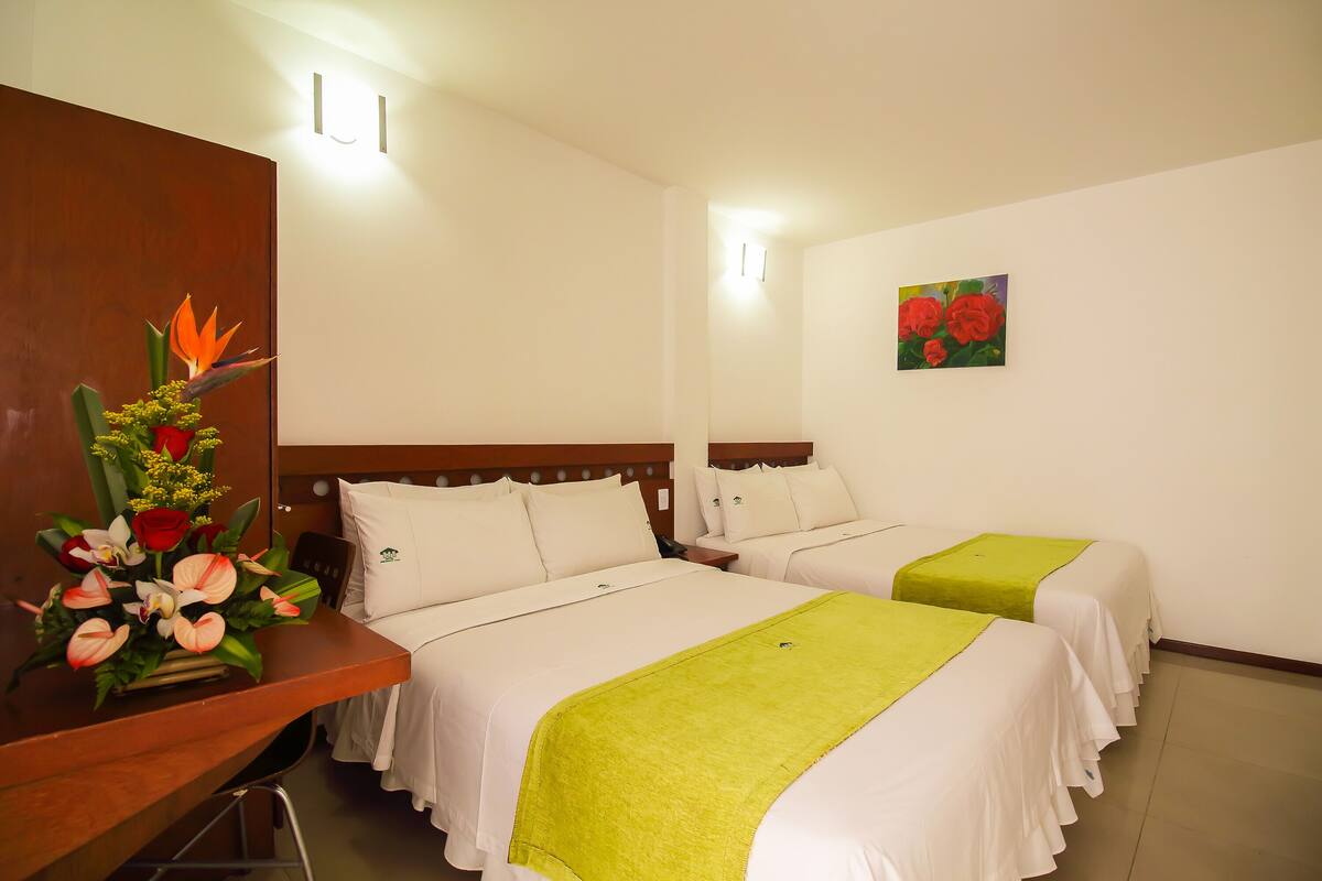 A hotel room with two beds, a wooden desk, and a floral arrangement.