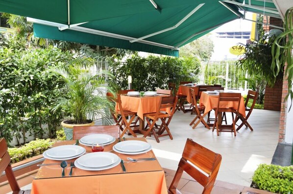 Un espace extérieur aménagé pour les repas, avec des tables et des chaises, entouré de verdure.