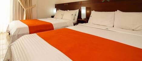 Dos camas matrimoniales con ropa de cama blanca y naranja, un cabecero de madera y una mesita de noche con una lámpara.